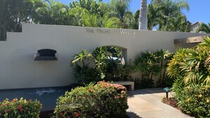 A landscaped area with a water feature, a wall with the text "The Palms at Wailea," and various tropical plants. - Beautiful - Palms at Wailea 1802 (Kihei)