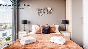 Ett hotellrum med en stor säng, två sängbord, ett fönster med utsikt över staden och en dekorativ väggdekoration.