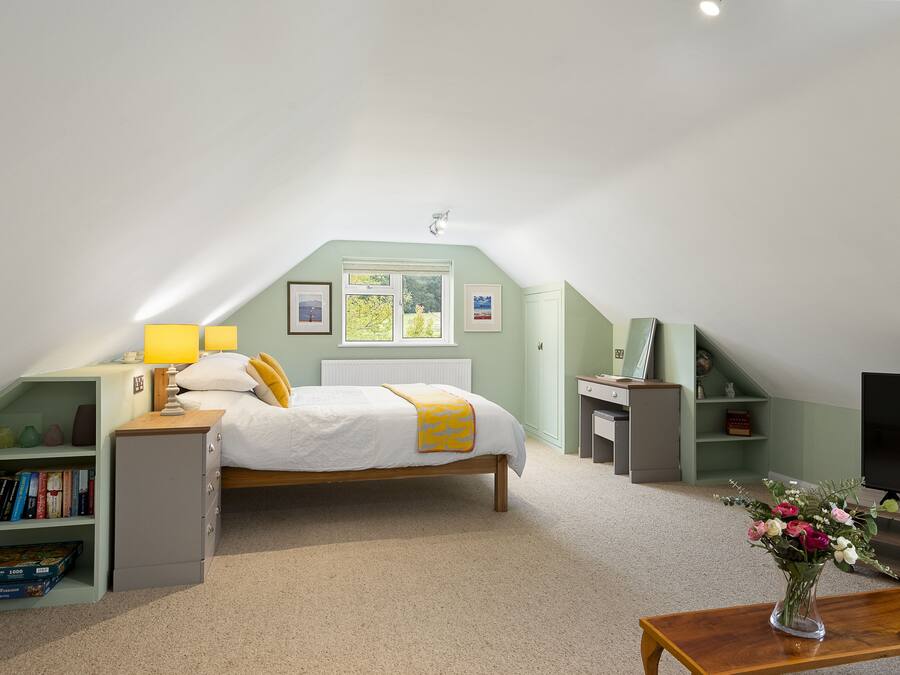 Un dormitorio con cama, mesita de noche, lámpara, estantería y televisor.