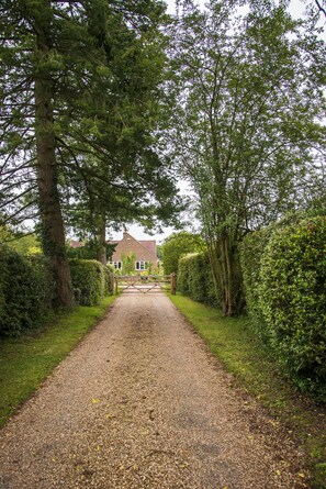 Une allée de gravier mène à une maison entourée d’une végétation luxuriante et d’arbres.