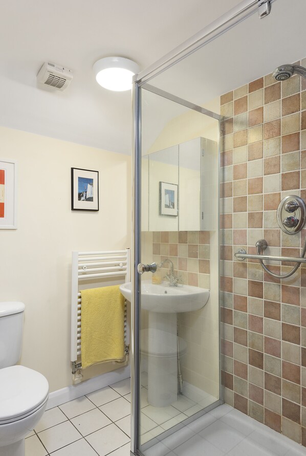 Une salle de bain avec une douche à parois de verre, un lavabo blanc, des toilettes et un porte-serviettes avec une serviette jaune.