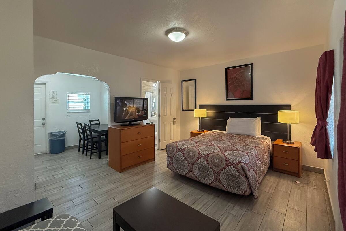 A hotel room with a bed, bedside tables, a TV, a desk, and a chair.