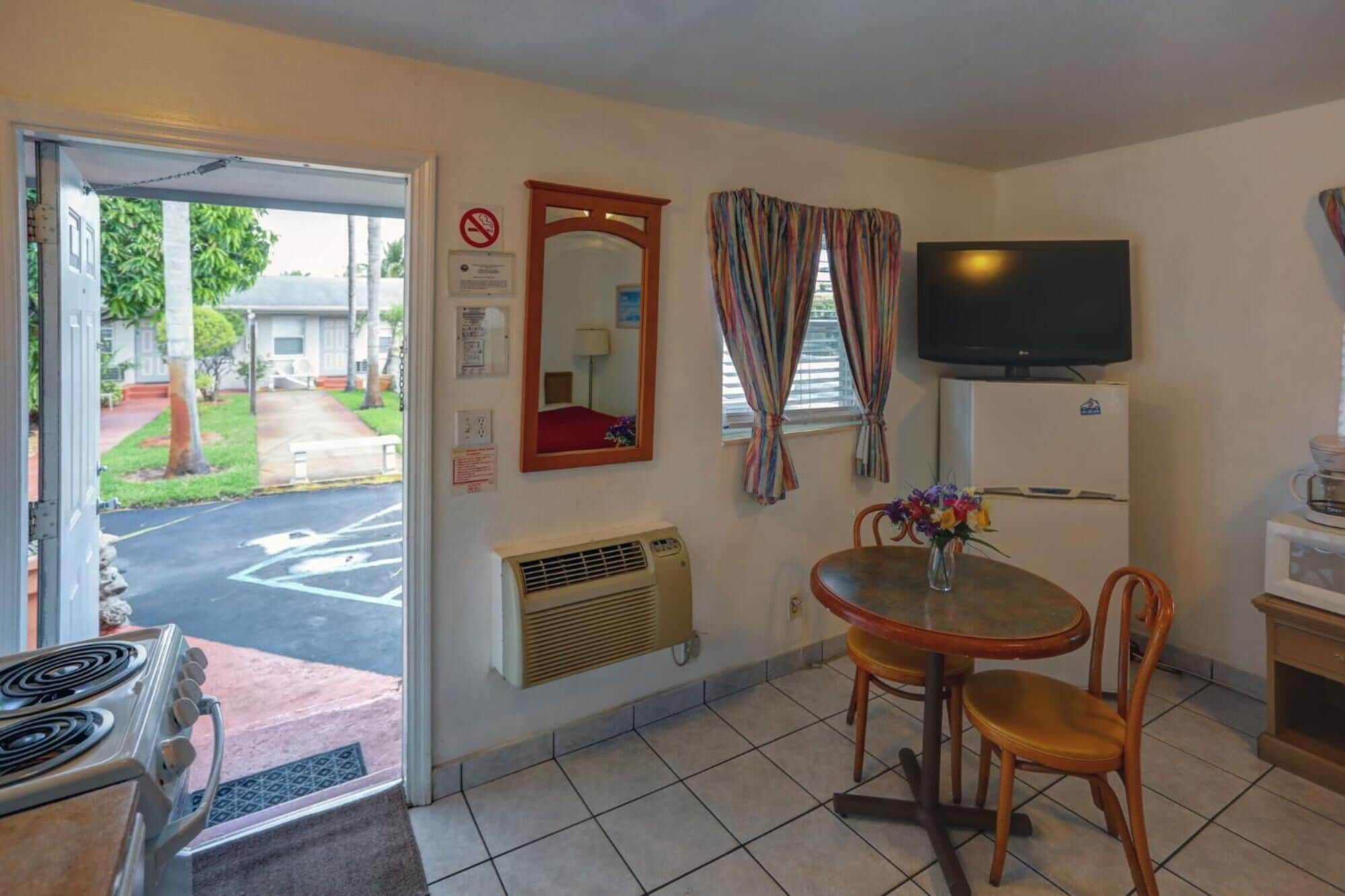 A compact kitchen with a stove, a dining table with chairs, a TV, and a refrigerator.