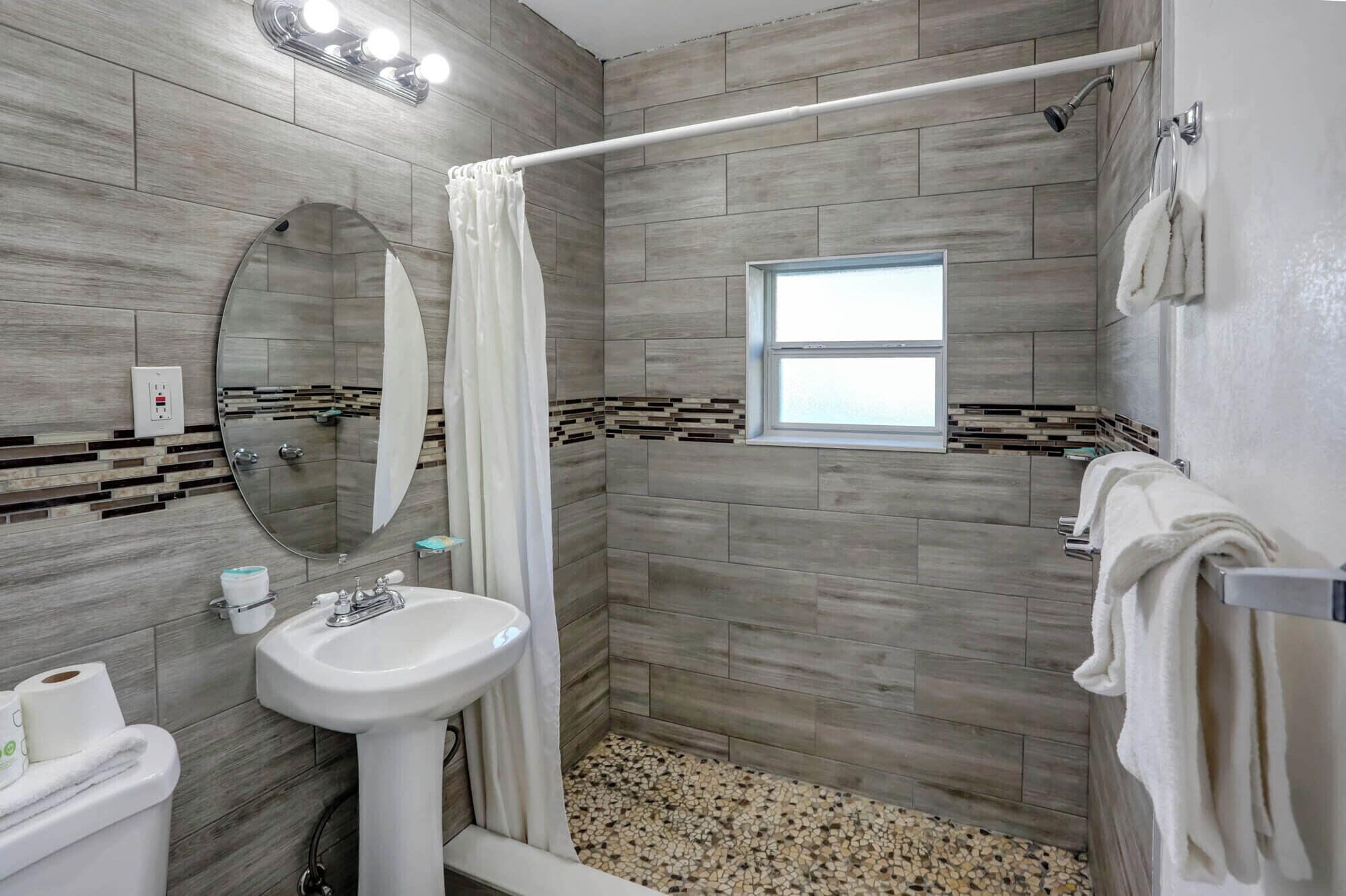 A modern bathroom with a shower, a sink, a mirror, and a window.