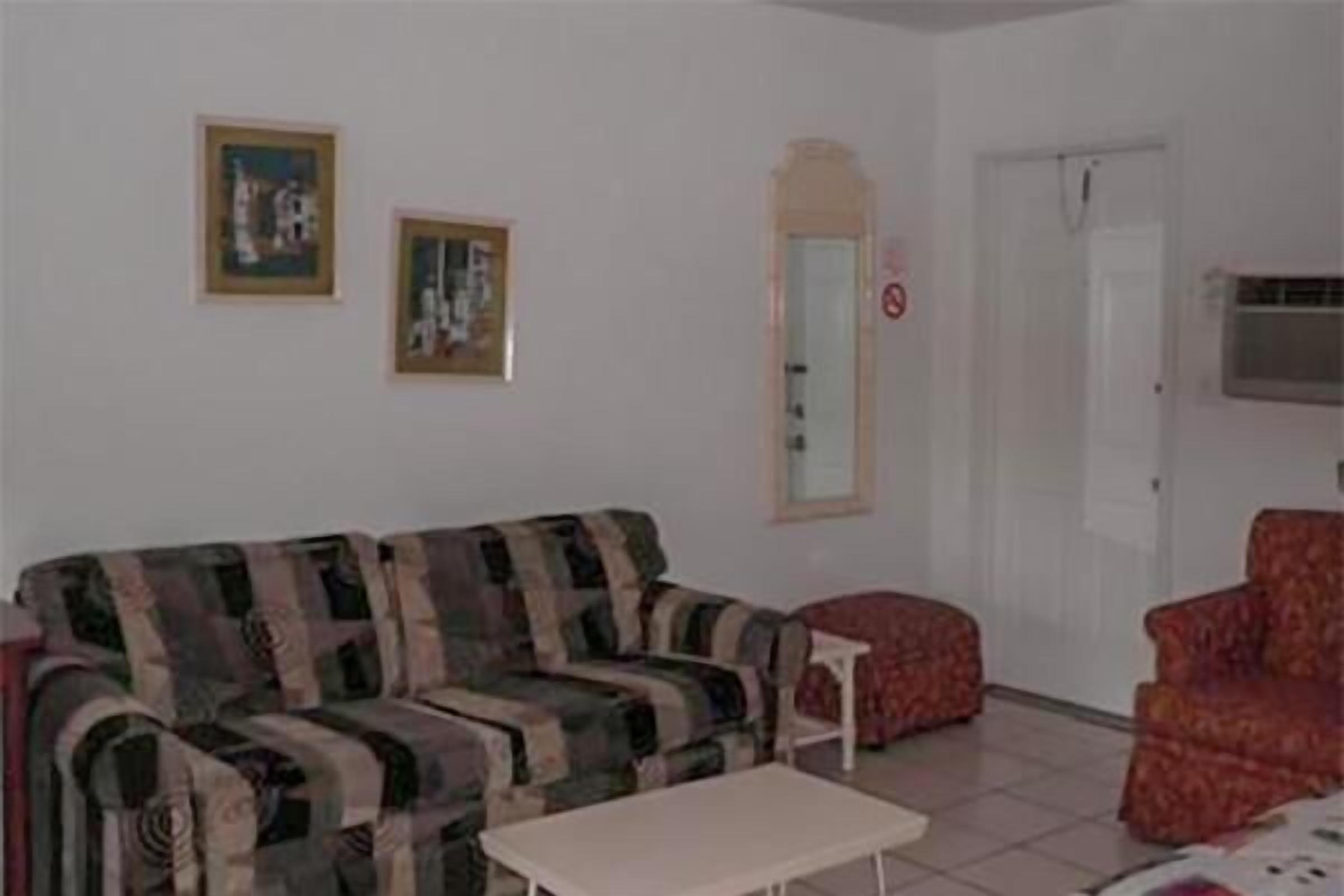 Ein Wohnzimmer mit einem gestreiften Sofa, einem kleinen weißen Tisch und einem roten Sessel. An der Wand hängen zwei gerahmte Bilder.