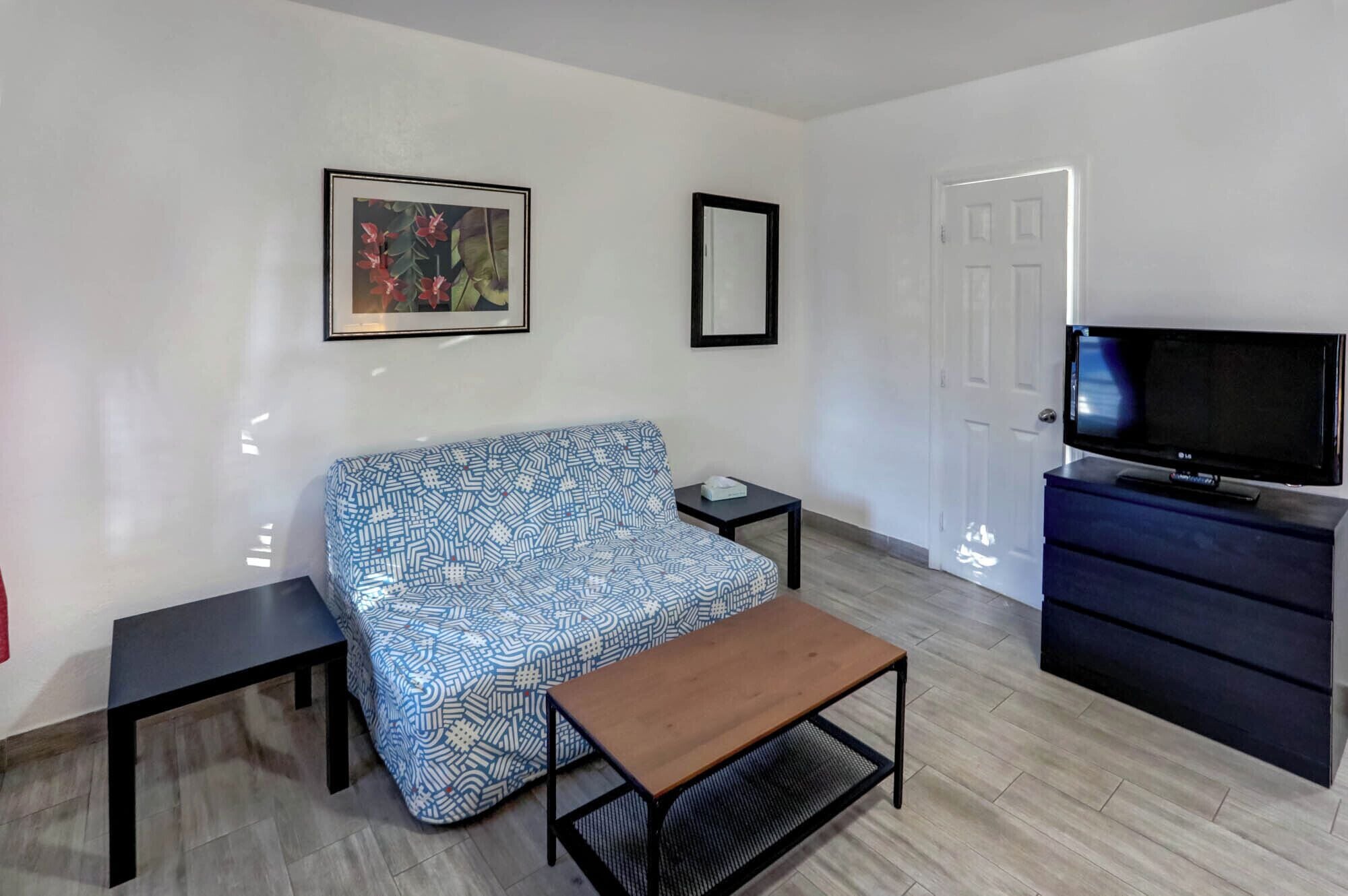 Una sala de estar pequeña y moderna con un sofá estampado, un banco de madera, un televisor y un aparador.