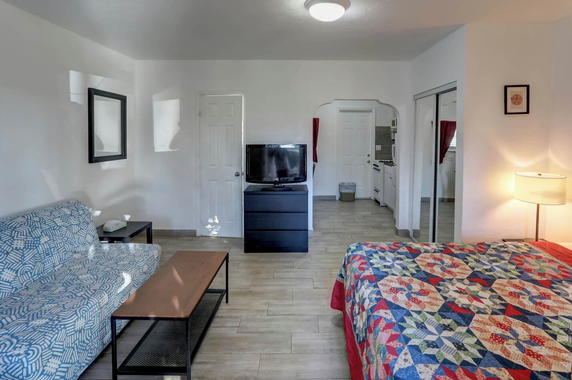 A hotel room with a bed, a sofa, a TV, a desk, and a kitchenette.