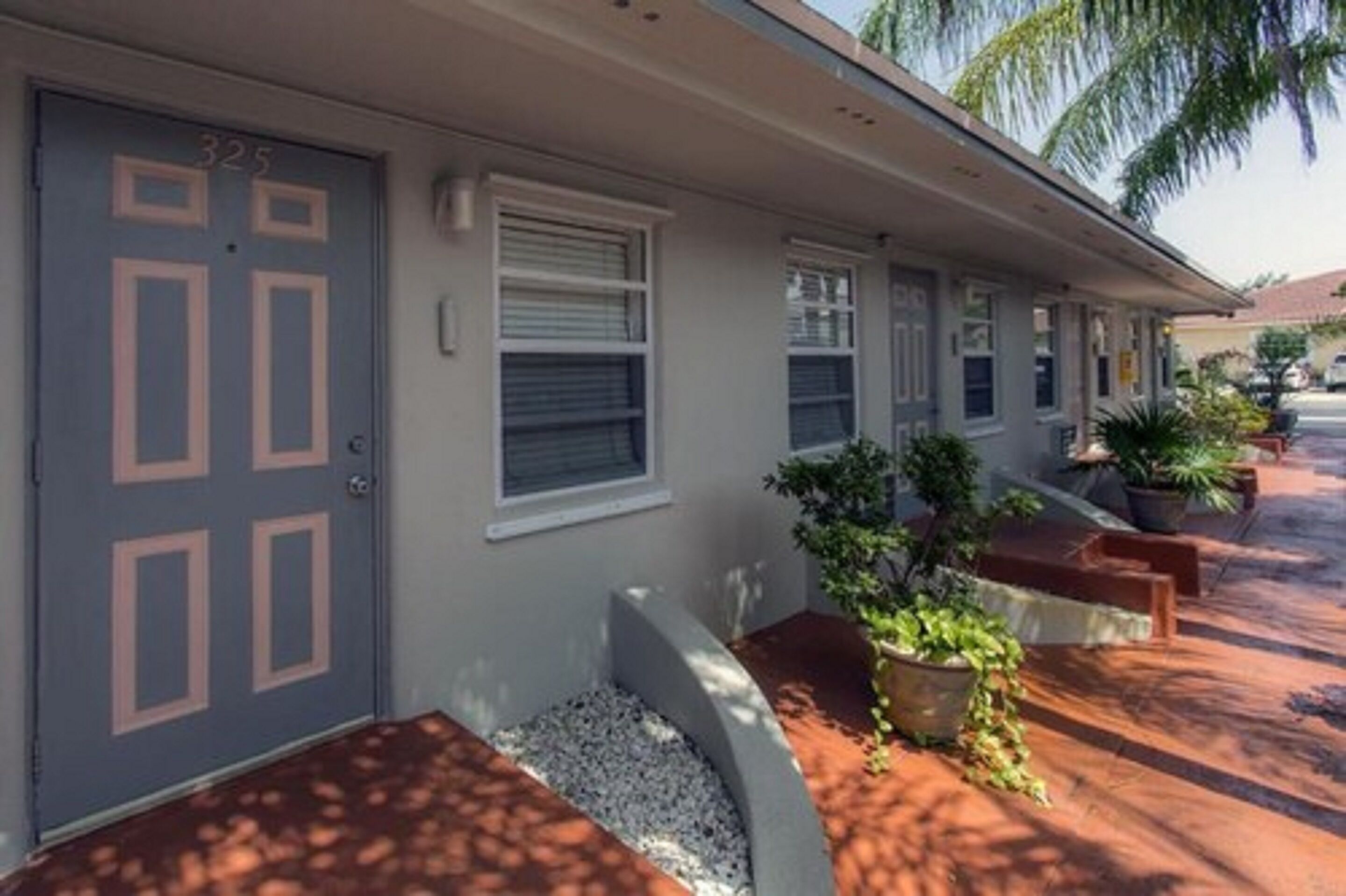 A row of motel rooms with a grey door marked "325", a covered walkway, and potted plants along the path.