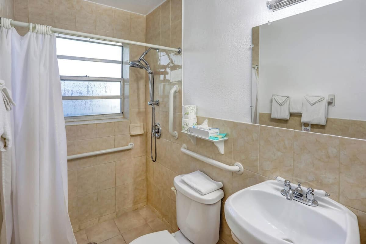 A bathroom with a shower, toilet, sink, and a window.