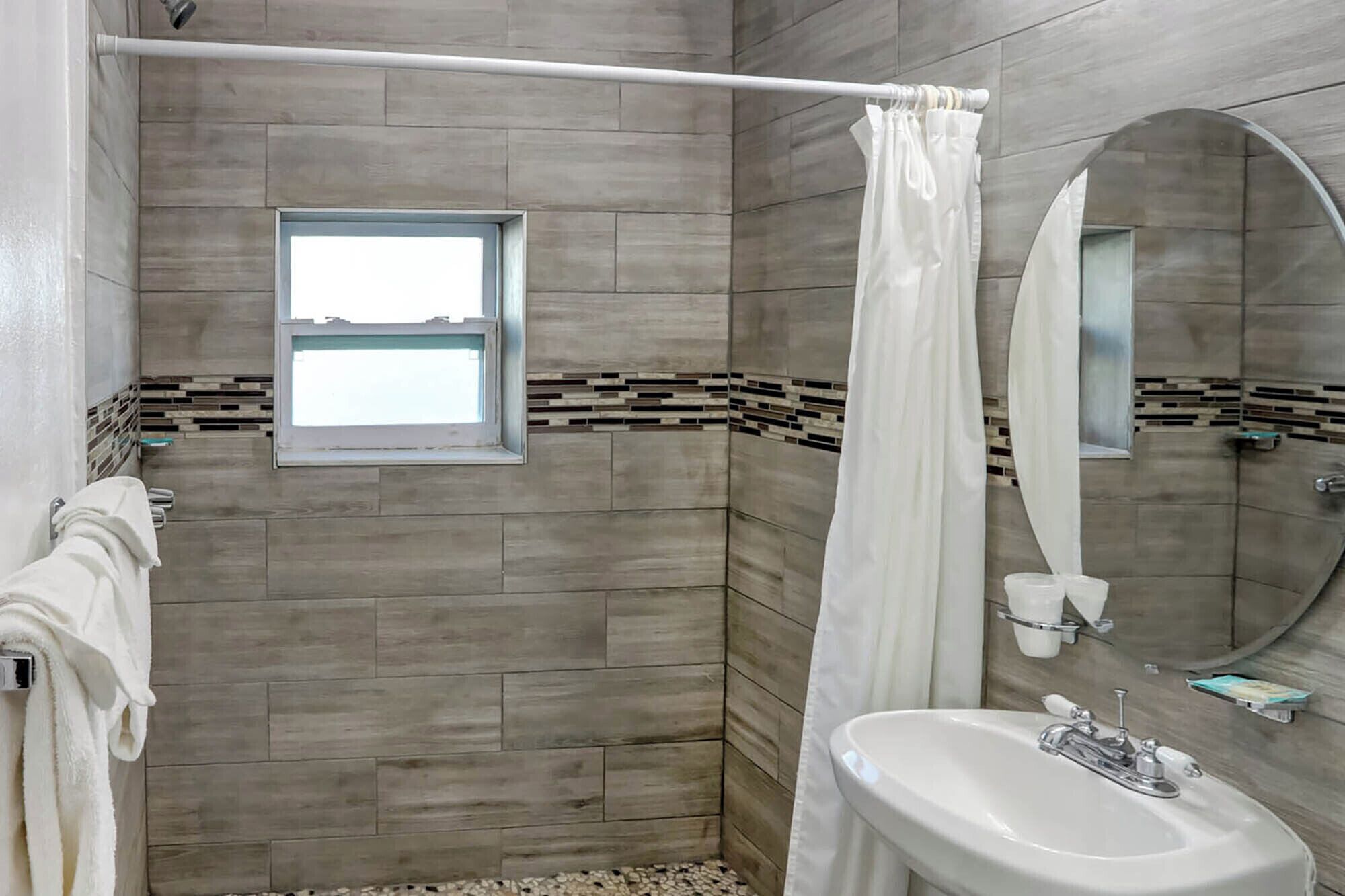 A modern bathroom with a shower, a window, a sink, and a mirror.