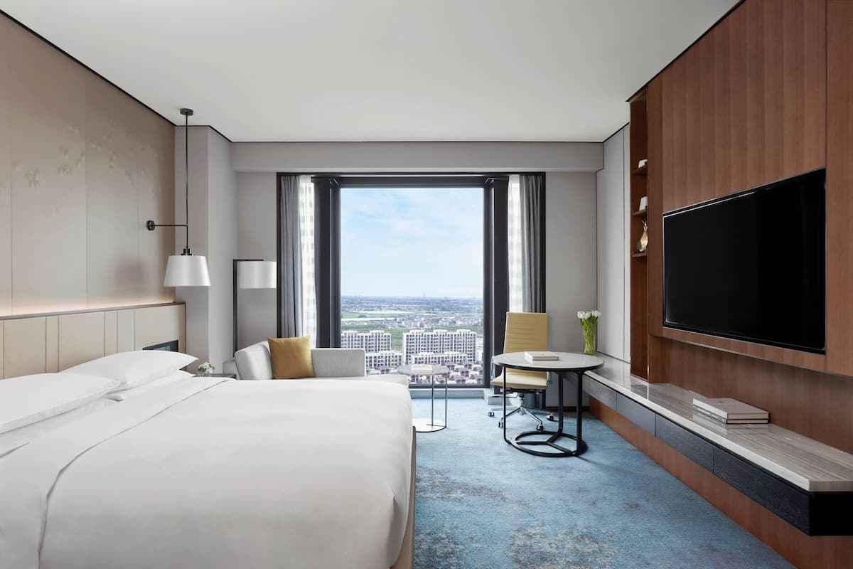 Une chambre d’hôtel dotée d’un grand lit, d’un bureau avec une chaise, d’un téléviseur à écran plat fixé au mur et offrant une vue sur la ville grâce à de grandes fenêtres.