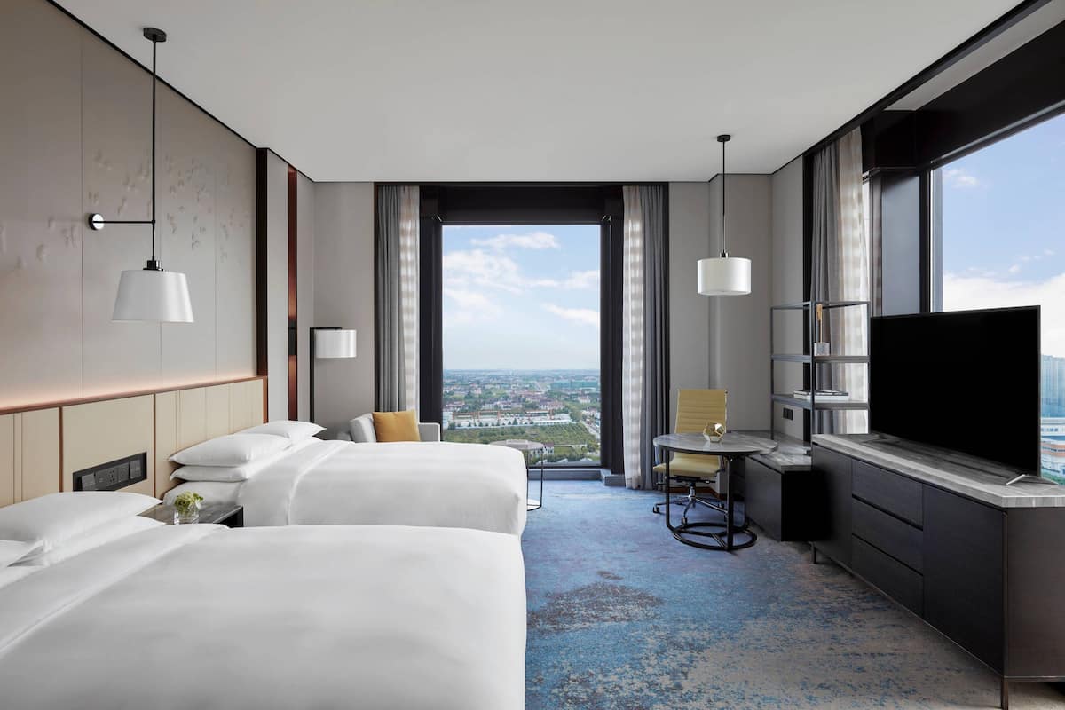 Une chambre d’hôtel avec deux lits, un bureau avec une chaise, une télévision et une grande fenêtre donnant sur la ville.
