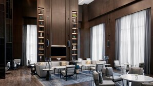 Een moderne hotellobby met een centrale zithoek, een grote flatscreen televisie en een boekenkast met decoratieve objecten.