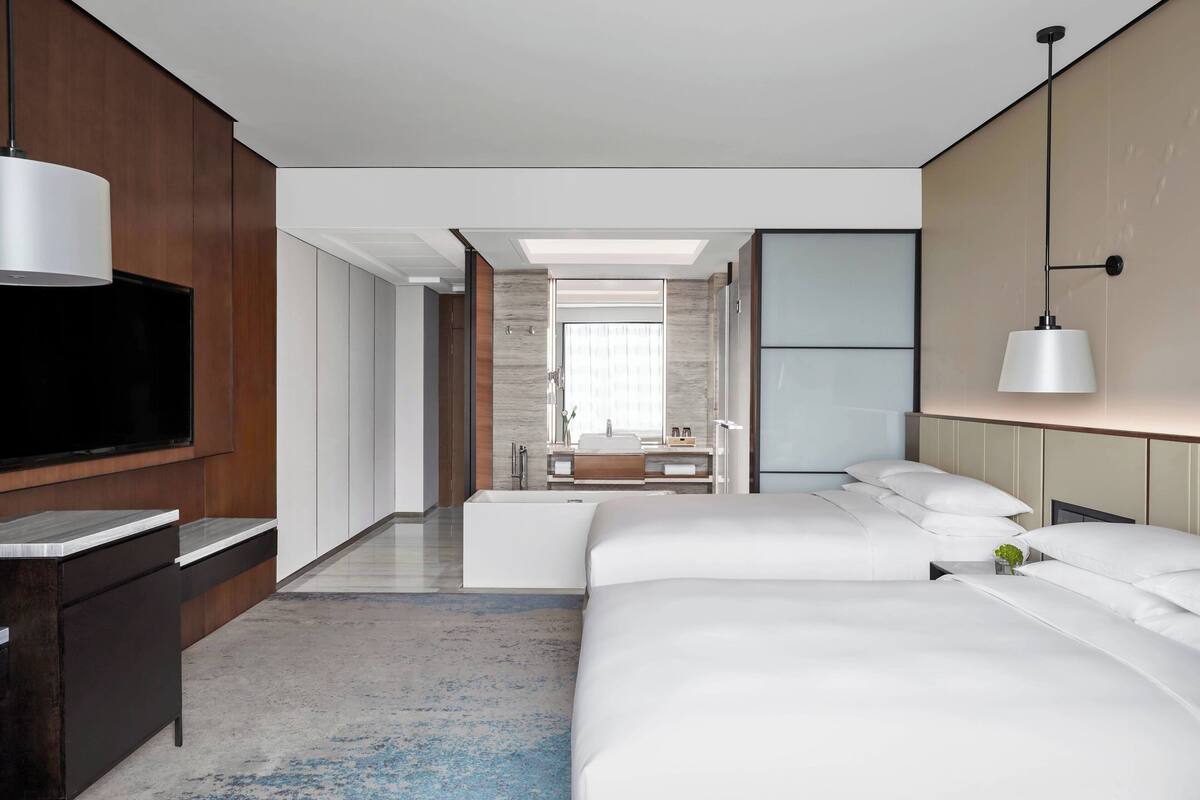 Une chambre d’hôtel moderne, dotée d’un grand lit, d’une télévision, d’un bureau et d’une salle de bain visible à travers une porte ouverte.