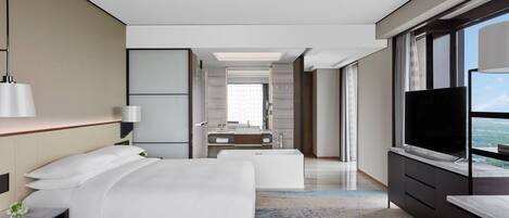 A modern hotel room with a large bed, a TV, a bathroom with a bathtub, and a view of the city.