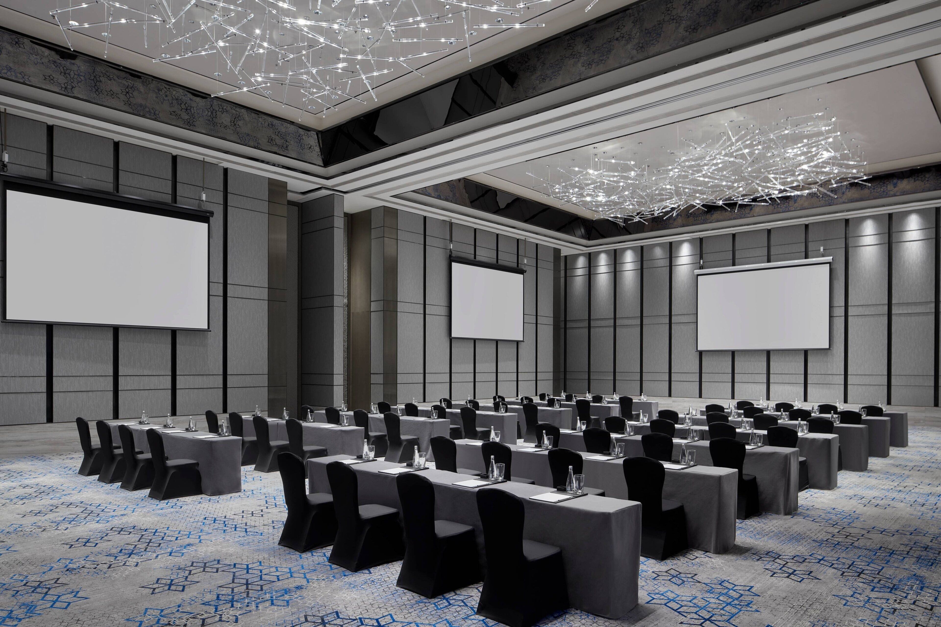 A conference room with multiple tables, chairs, and large screens.