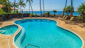 Ein Pool mit geschwungener Kante, umgeben von Liegestühlen und Sonnenschirmen, mit Blick auf den Ozean und Palmen.