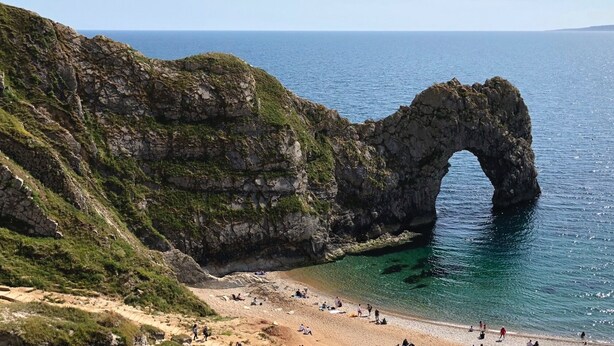 Un paisaje costero con una imponente formación rocosa en arco, una playa de arena y aguas azules cristalinas.