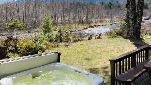 A hot tub on a wooden deck with a view of a river and mountains in the background.