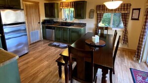 A compact kitchen with wooden cabinets, a built-in microwave, and a dishwasher. There's a dining table with chairs and a hanging light fixture.