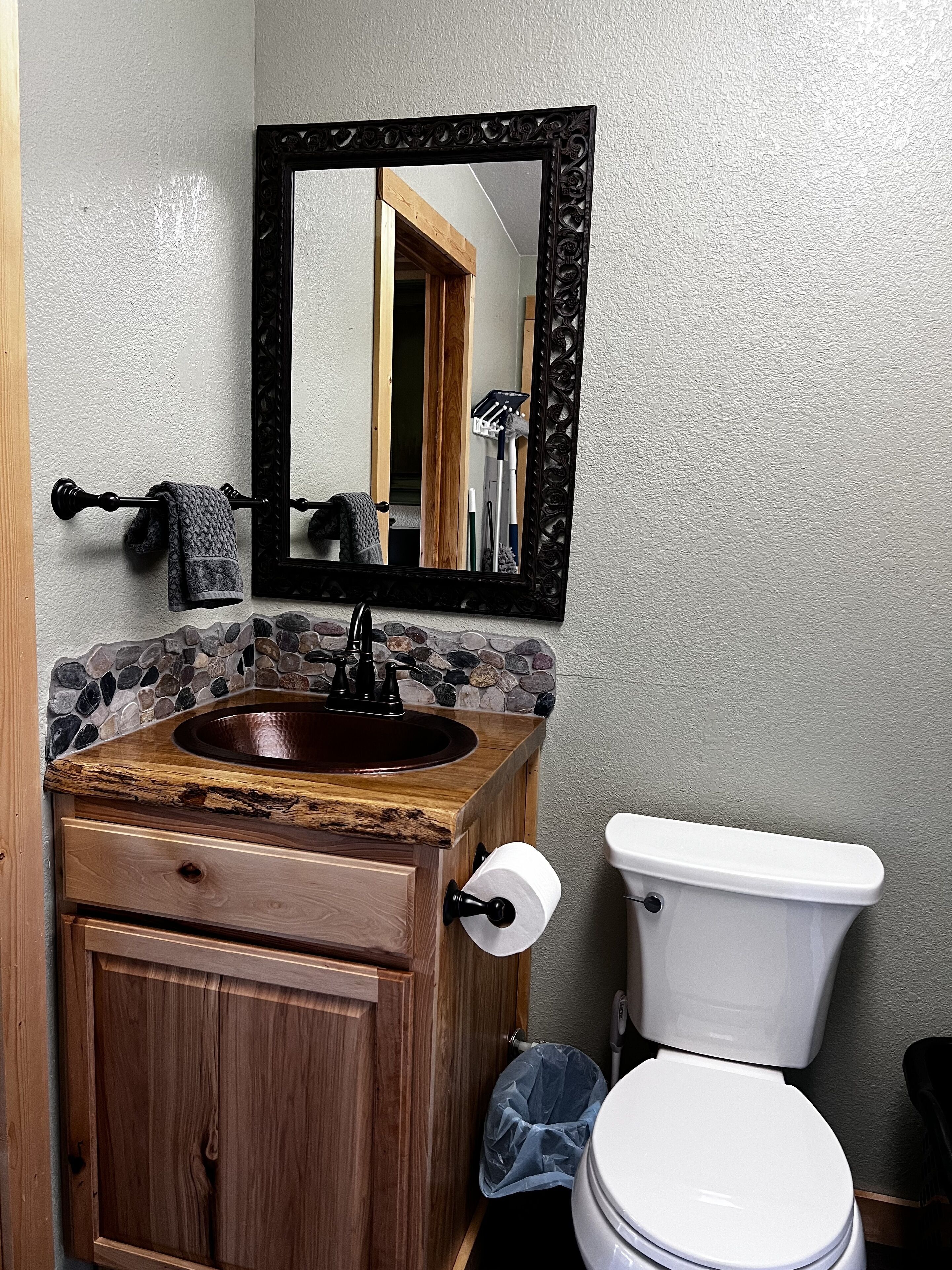 Ein Badezimmer mit einem Holzauszug, einer Stein-Mosaik-Rückwand, einem spiegelüberspannten schwarzen Rahmen, einer weißen Toilette und einem Handtuchhalter mit einem Handtuch.