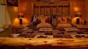 A cozy room with a bed featuring a forest-themed quilt, two nightstands with lamps, and a wooden headboard.