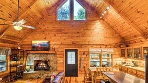 A cozy cabin interior with a stone fireplace, wooden walls, a dining area, and a large window. - Blue Ridge - Creek Front Paradise w/great outdoors (Blue Ridge)