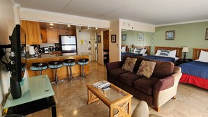 Una habitación de hotel compacta con kitchenette, un sofá, una cama y una pequeña mesa.