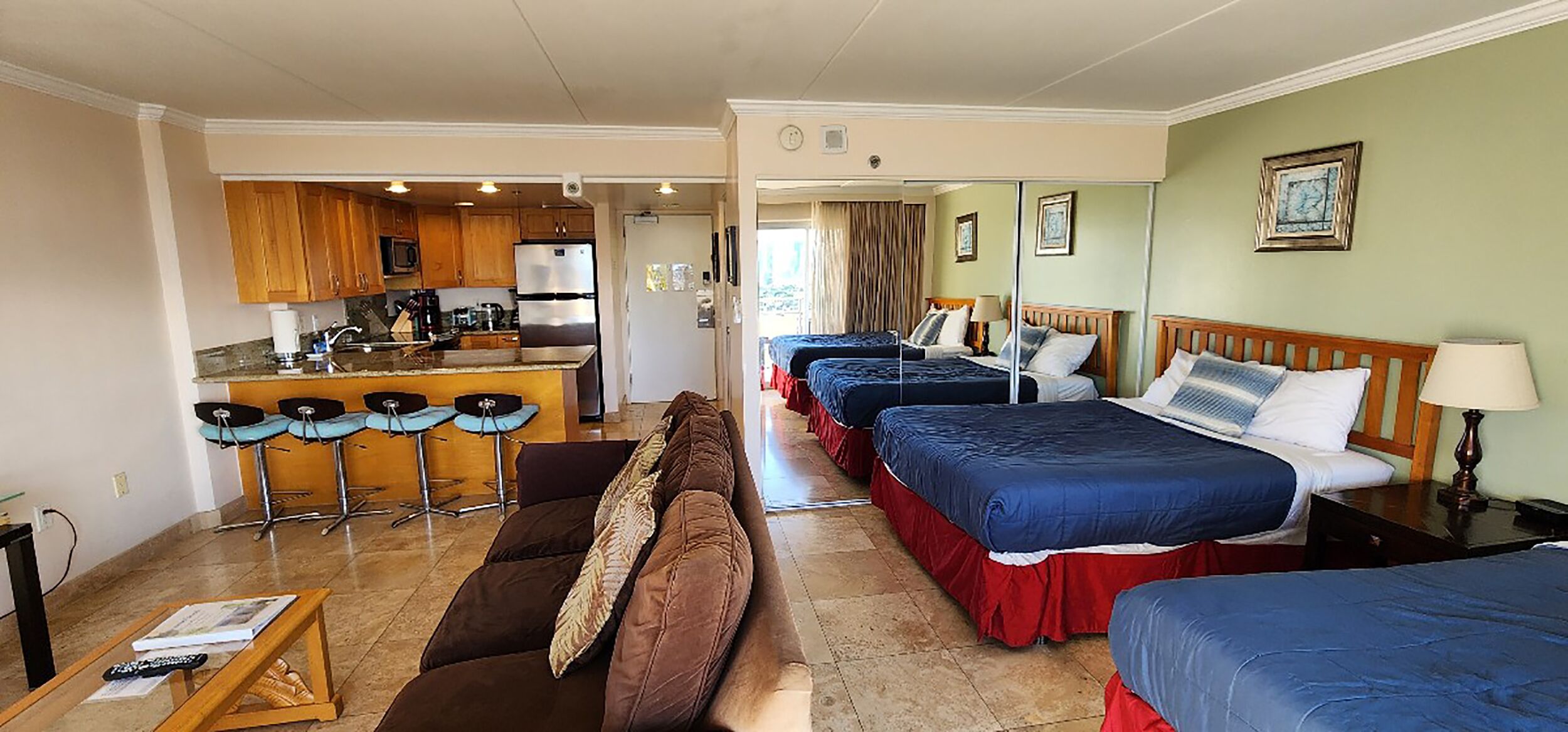 A hotel room with a kitchenette, two beds, a sofa, and a dining area.