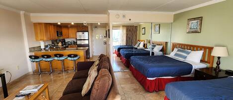 A hotel room with a kitchenette, two beds, a sofa, and a dining area.