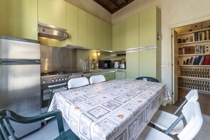 A compact kitchen with a dining table, chairs, a bookshelf, and a stove.