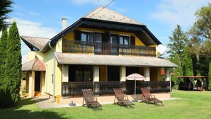 A two-story house with a balcony, a covered patio with chairs, and a well-maintained lawn. - Vacation home Akazie by Interhome (Balatonmariafurdo)