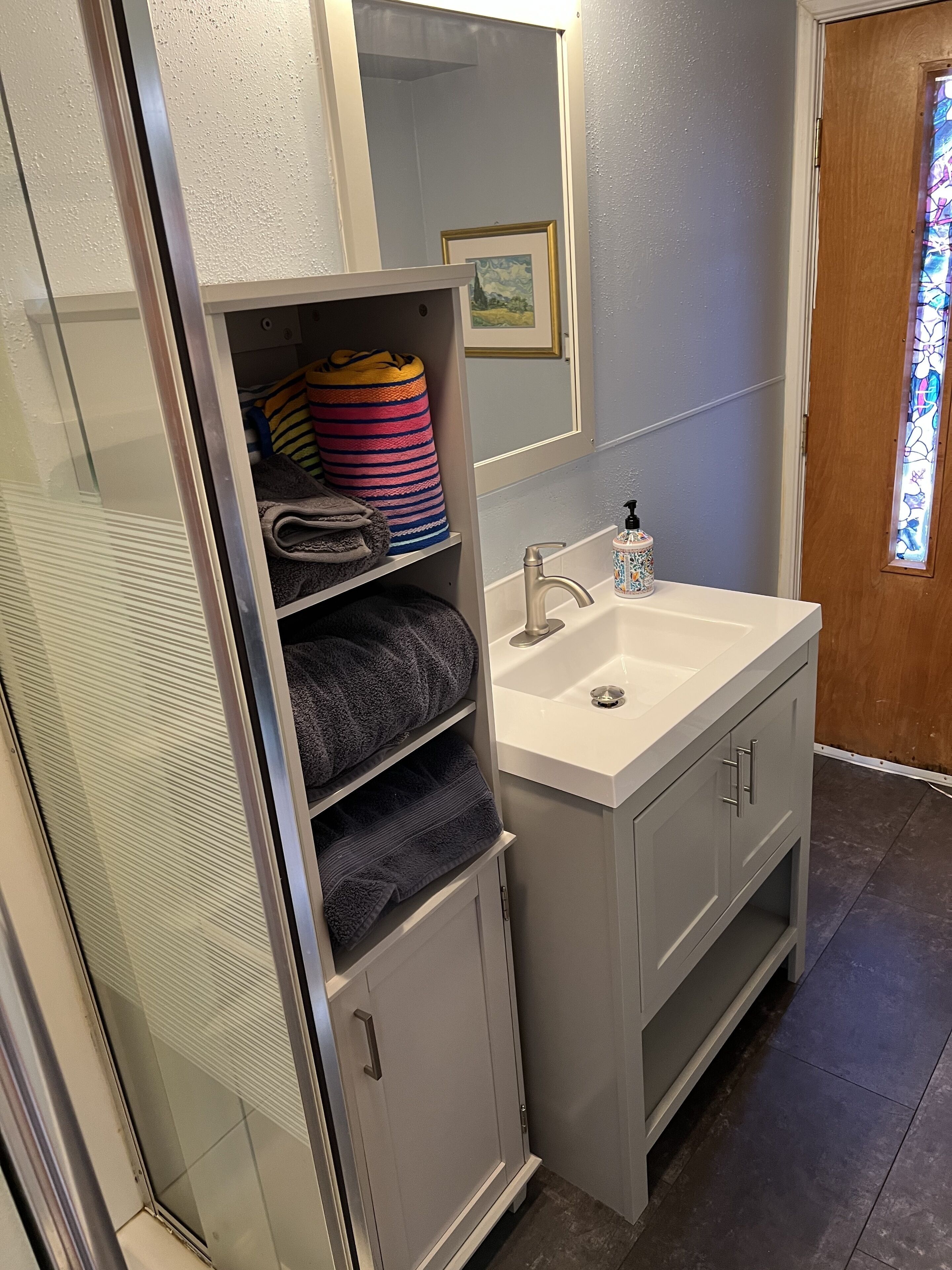 A bathroom with a white sink, a mirror, and a towel rack with folded towels.