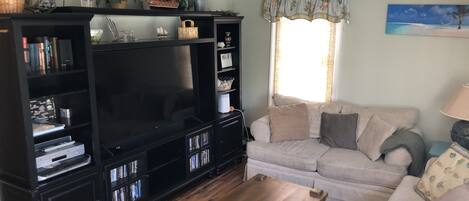 Una sala de estar con un mueble multimedia negro grande, un sofá color crema y una mesa de centro de madera.