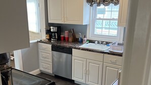 A kitchen with white cabinets, a black stove, and a window with patterned curtains. - Beach House in Ocean Beach, Fire Island (Ocean Beach)