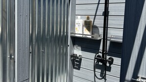 A wooden deck with a showerhead and a water tank in the background. - Beach House in Ocean Beach, Fire Island (Ocean Beach)