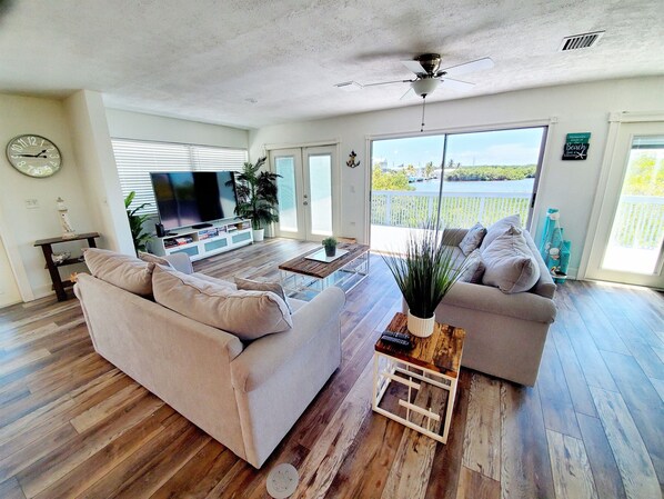 A spacious living room with a large flat-screen TV, two sofas, a coffee table, and a ceiling fan.