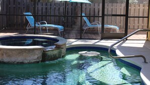 Una piscina con un pontile in legno, due lettini e un ombrellone blu.