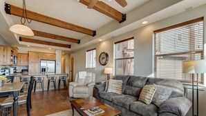 Amplia sala de estar con un sofá gris, vigas de techo de madera y un comedor con mesa y sillas de madera.