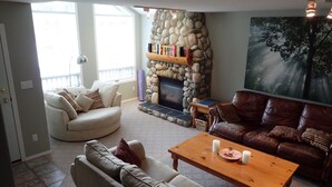 A living room with a stone fireplace, two sofas, a coffee table, and a large window. - Fernie Alpine Resort accommodation Thunder Ridge Chalet Truely Ski in/Ski out  (Fernie)