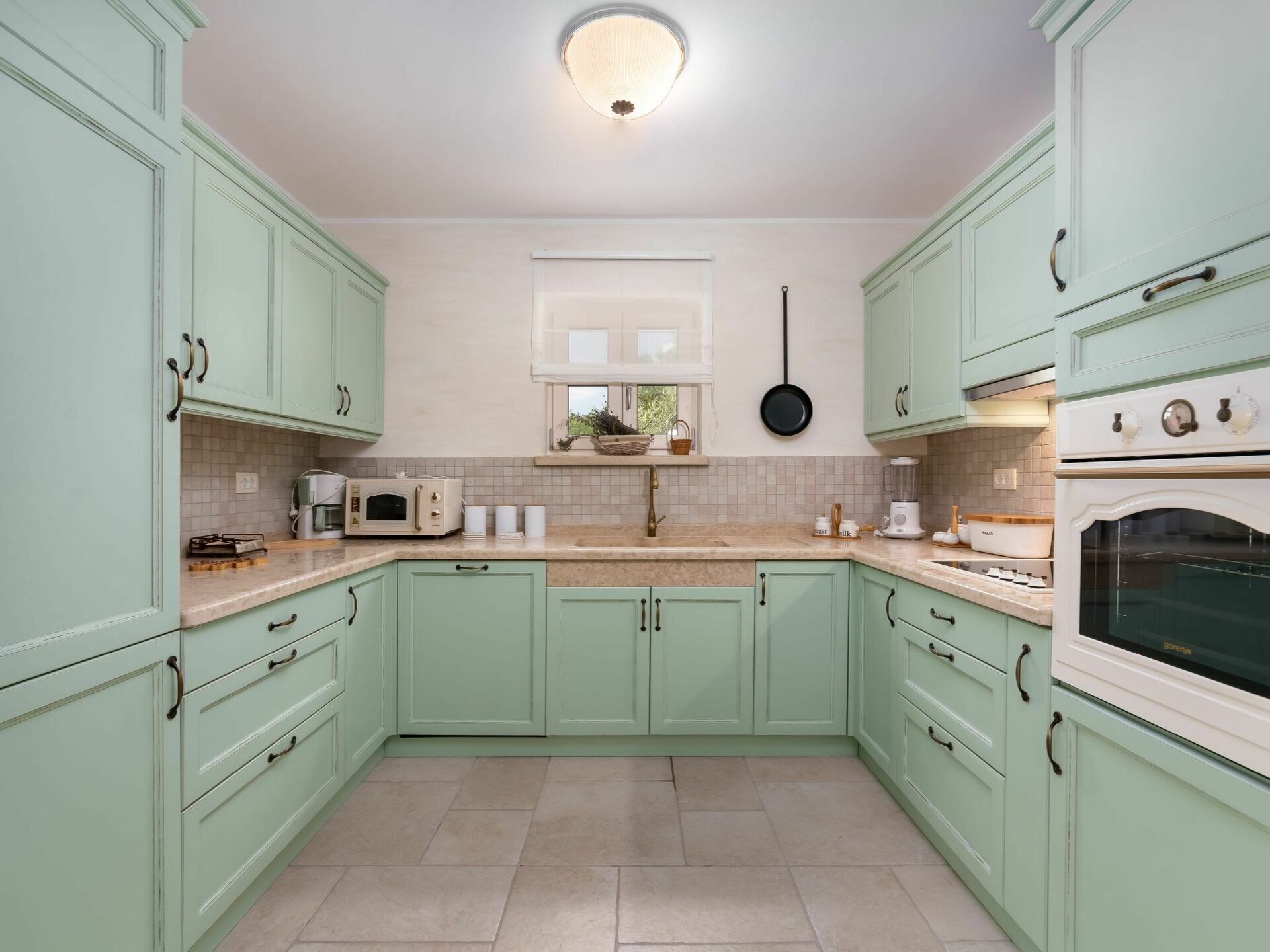 A kitchen with light green cabinets, a white stove, and a window above the sink.