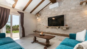 A modern living room with a stone wall, a flat-screen TV, a wooden coffee table, and teal sofas. - Beautiful private villa for 6 people with WIFI, private pool, A/C, TV, terrace and pets allowed (Pazin)