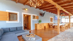 A spacious living area with a wooden ceiling, a sofa, a coffee table with magazines, a kitchen area with wooden cabinets, and a dining table with chairs. - Pool & Fun House Betiga 1 With Gym, Fažana, Croatia (Fažana)