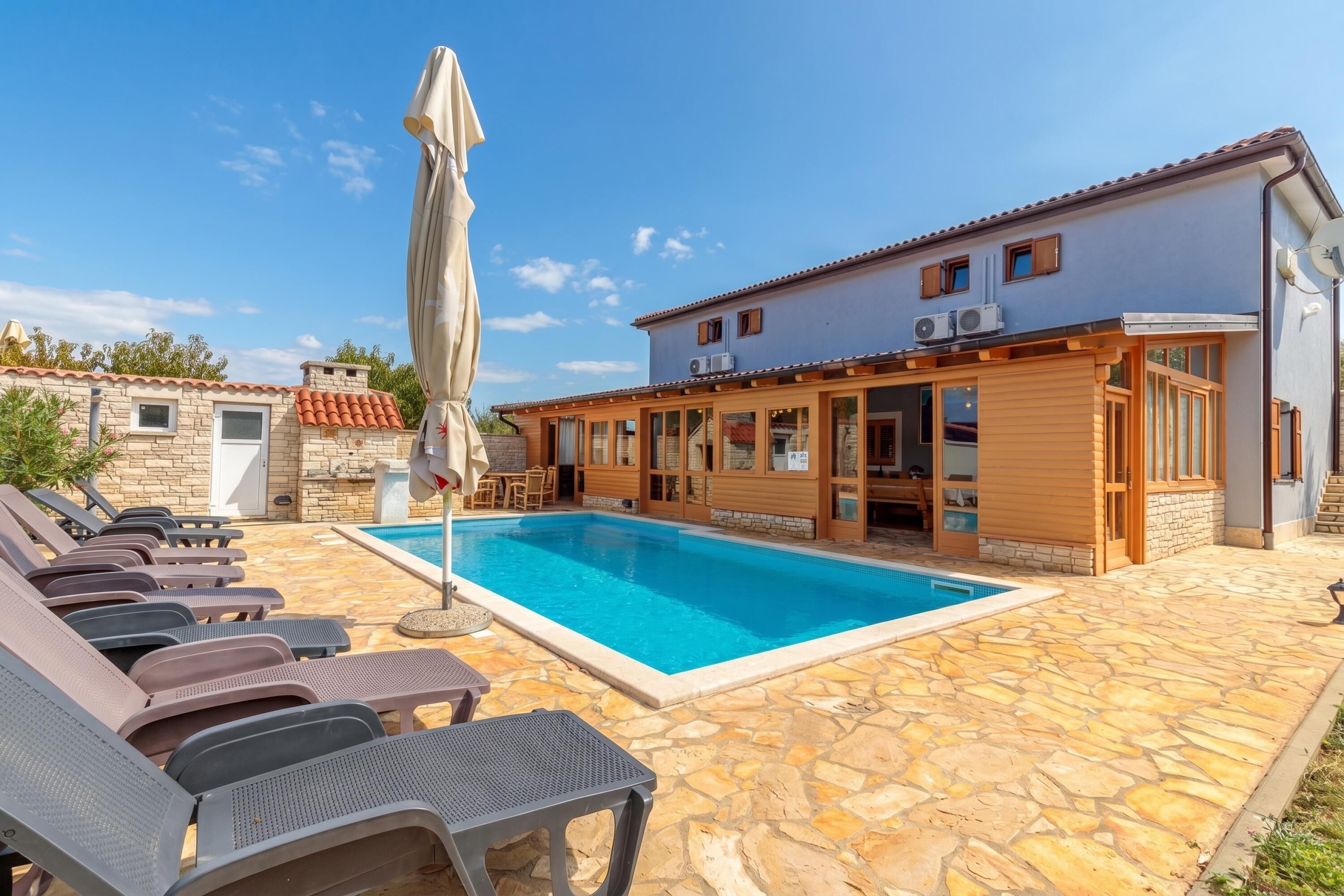 A poolside area with lounge chairs, a pool, and a building with a tiled roof and wooden deck.