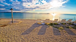 A pebbled beach with lounge chairs and a sun umbrella. - Pool & Fun House Betiga 1 With Gym, Fažana, Croatia (Fažana)