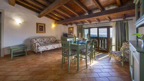 A cozy room with a wooden ceiling, a dining table with chairs, a sofa, and a view through a window.
