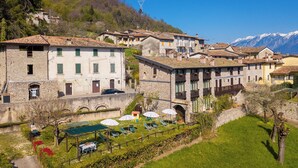 A hillside village with stone buildings, a paved path, and a grassy area with outdoor seating.