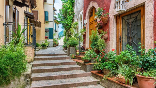 A narrow cobblestone street with steps leading to a building with a wooden door and a window with a metal grill.