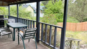 A covered deck with a table and chairs, a grill, and a view of a backyard with a wooden fence and greenery. - Entire Home & Fenced Yard For Family & Pets (Independence)