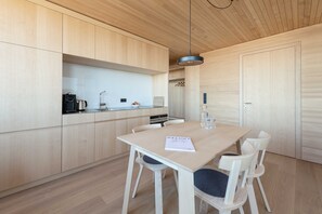 A modern kitchen with wooden cabinets, a dining table with chairs, and a pendant light. - Apartment 1 - Apartments Poldi (Sulzberg)